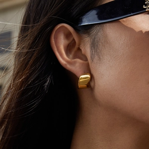 Close-up of a model wearing high-polish thick golden C-hoop stainless steel earrings