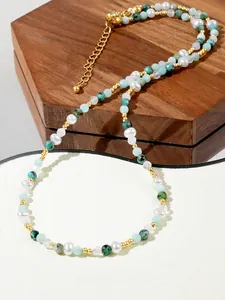 Detail of bohemian necklace with blue beads, green stones and gold spacers on wooden stand