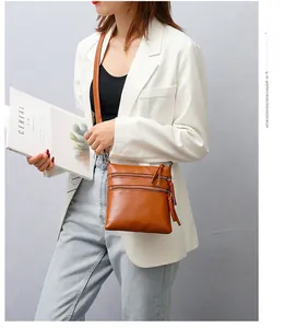 Brown leather crossbody phone bag with three zipper pockets shown on a white blazer outfit