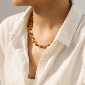 Close-up of a gold knotted link necklace on a model wearing a professional white shirt