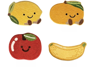 Detail view of four fruit-shaped plush bath mats with cute cartoon faces and soft textures
