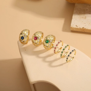 Detail shot of six gold-plated zircon rings in blue, red, and green on a beige stand