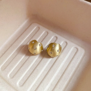 Detailed close-up of matte gold spherical earrings with star-patterned crystals in a tray