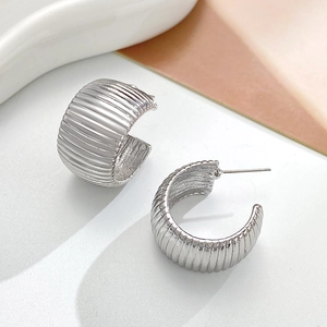 Close-up of silver metal C-shaped earrings with vertical textured stripes and polished finish
