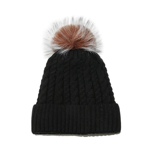Detailed view of the thick cable knit pattern and fluffy faux fur pompom on this black winter hat