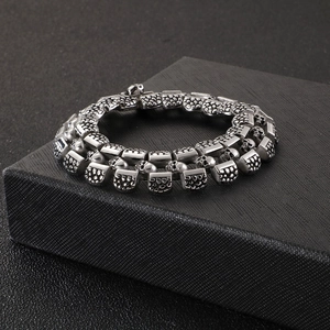 Punk style silver stainless steel bracelet featuring detailed skull links on black stand