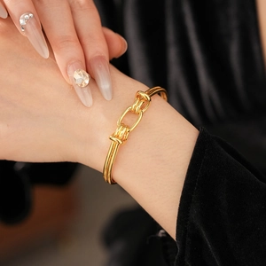 Close-up of a gold-plated oval knot cuff bracelet on a model against a black background