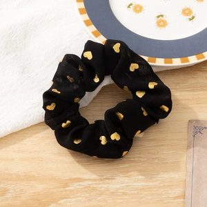 Black fabric hair scrunchie with gold heart patterns on a rustic wooden table surface