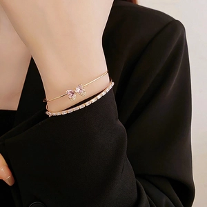 Close-up of a gold bangle with a pink crystal butterfly and a baguette zircon bracelet
