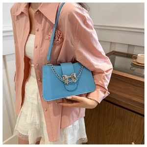 Close-up of light blue shoulder bag with silver metal chain and bow buckle detail