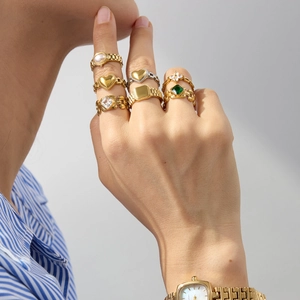 Stackable gold stainless steel rings set with emerald and pearl accents on model's hand