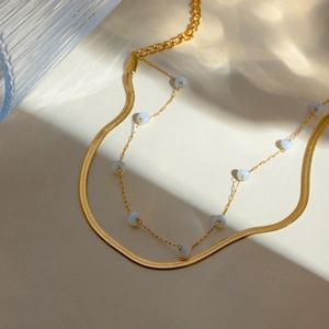 Detail of 18K gold double-layer anklet with sleek snake chain and white pearl beads