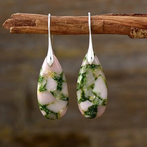 Detail of bohemian teardrop earrings with pink and green stone texture on wood