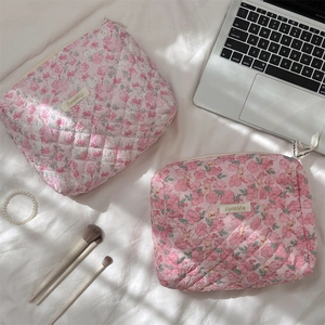 Detailed view of pink floral quilted makeup bags set on a white cozy bed background