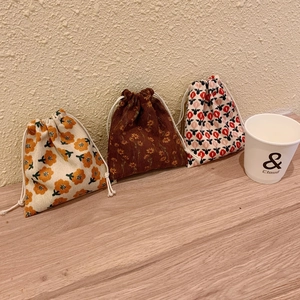 Detailed view of three corduroy drawstring pouches with floral patterns on a wooden surface