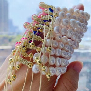 Handheld stack of rainbow pearl bracelets with gold beads and beige woven drawstrings