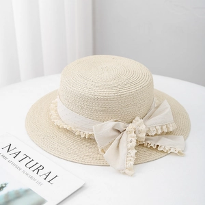 Flat top cream straw hat with lace ribbon and bow tie on white table with a magazine