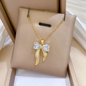 Detailed shot of golden bow necklace with heart-shaped zircons on beige jewelry cushion
