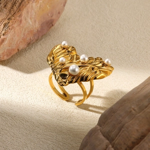 Macro detail of leaf-shaped gold ring featuring five pearls on textured stone