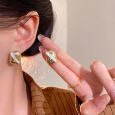 Detail view of rectangular gold earrings with white diagonal stripes on a model ear