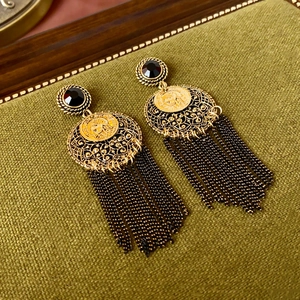 Detail of vintage bohemian tassel earrings with gold coin relief and black gems on velvet