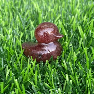 Detailed view of dark reddish-brown gemstone duck figurine on green grass