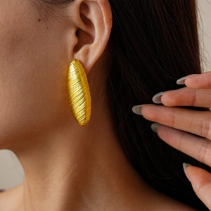 Close-up of a model wearing a golden oval earring with textured brushed metal finish