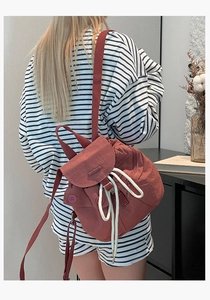 Macro view of rust red nylon drawstring backpack with white ropes on a model