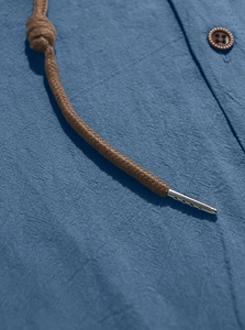 Detail of blue cotton-linen shirt featuring brown braided drawstrings and wood-tone buttons