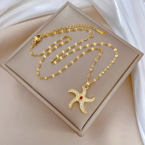 Gold rotating starfish necklace with red crystals on a beige jewelry box with silk