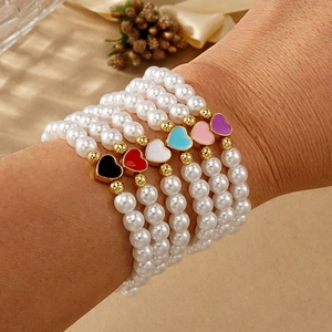 Detalle de pulseras de perlas en capas con cuentas doradas y corazones de esmalte