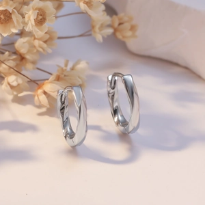 Minimalist silver twist hoop earrings with a sleek polished finish on a natural background