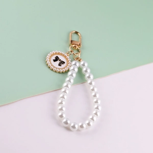 Handmade white glass pearl wrist strap keychain with gold lobster clasp on bicolor background