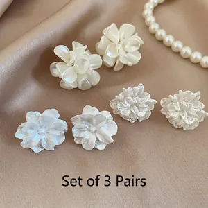 Set of 3 pairs of white floral stud earrings with pearl and resin textures on beige silk