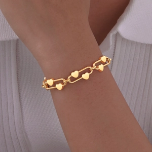 Detail shot of a golden paperclip link bracelet with 3D heart charms worn on a wrist