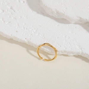 Close-up of golden wavy open ring featuring zircon pave setting on stone background
