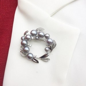 Detailed shot of a silver flower brooch with grey freshwater pearls on white fabric