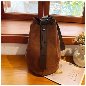 Close-up of brown suede bucket bag with wide leather strap on a wooden windowsill