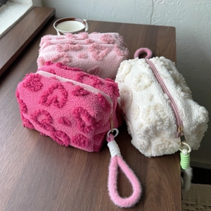 Three plush floral makeup bags in pink and white on a wooden table with soft lighting