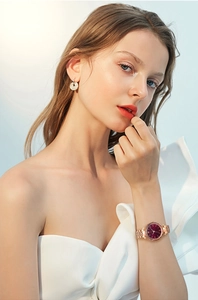 Close-up of rose gold watch with burgundy dial worn by a model with silver earrings