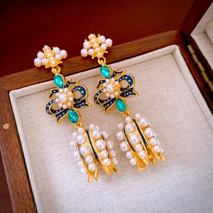 Macro view of vintage-style gold earrings with pearls, blue enamel, and green gemstones