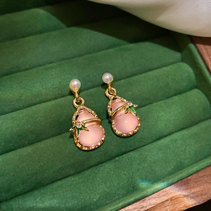 Close-up of pink gourd earrings with gold edges, pearls and green leaf accents