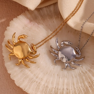 Polished 18K gold and silver crab pendant necklaces displayed on a coral base
