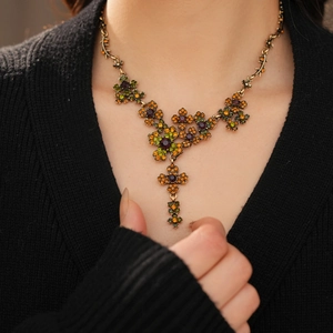 Détail d'un collier fleur vintage en bronze avec cristaux colorés sur un pull noir élégant