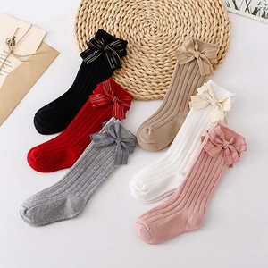 Kids knee high socks with gold edge bows in six colors displayed on woven mat