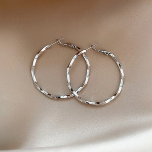 Detailed shot of silver geometric C-shape hoop earrings on elegant champagne silk fabric
