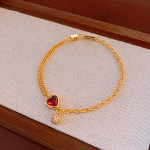 Close-up of gold heart bracelet with red gemstone and micro-pave zircon ball charm