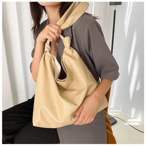 Beige soft PU leather tote bag with unique knotted handle shown on model in grey suit