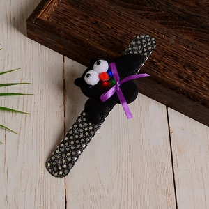 Detail of Halloween sequined snap bracelet with plush bat figure on a wooden surface