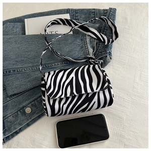 Detailed view of a zebra print crossbody bag on textured fabric with lifestyle props